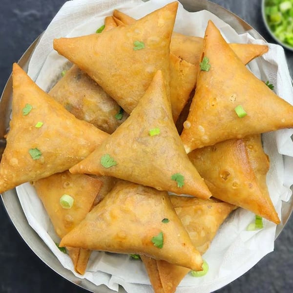 A close-up of golden-brown, triangular samosas garnished with fresh herbs in a metal bowl.