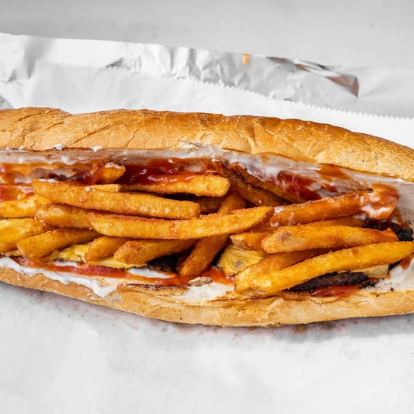 A close-up of a halal sandwich filled with french fries, meat, cheese, and sauces.