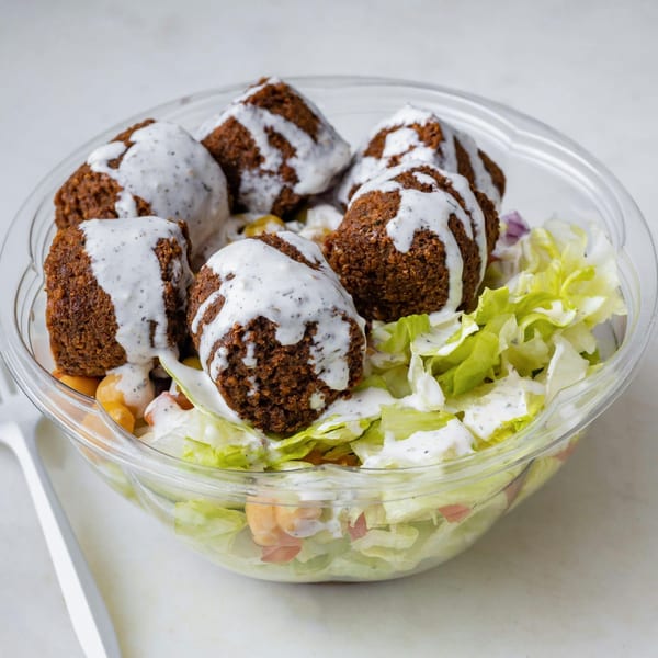 A clear plastic bowl filled with falafel, lettuce, and chickpeas, drizzled with white sauce.