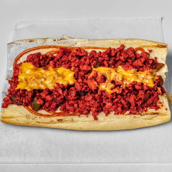 A halal cheesesteak sandwich with bright red meat, melted cheese, and sauce on a white background.