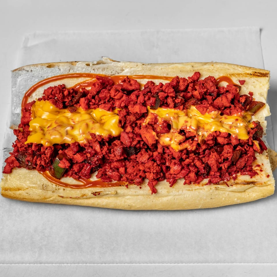 A halal cheesesteak sandwich with bright red meat, melted cheese, and sauce on a white background.