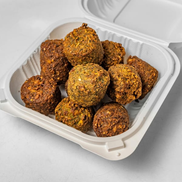 A white takeout container filled with a dozen golden-brown falafel balls, ready to eat.