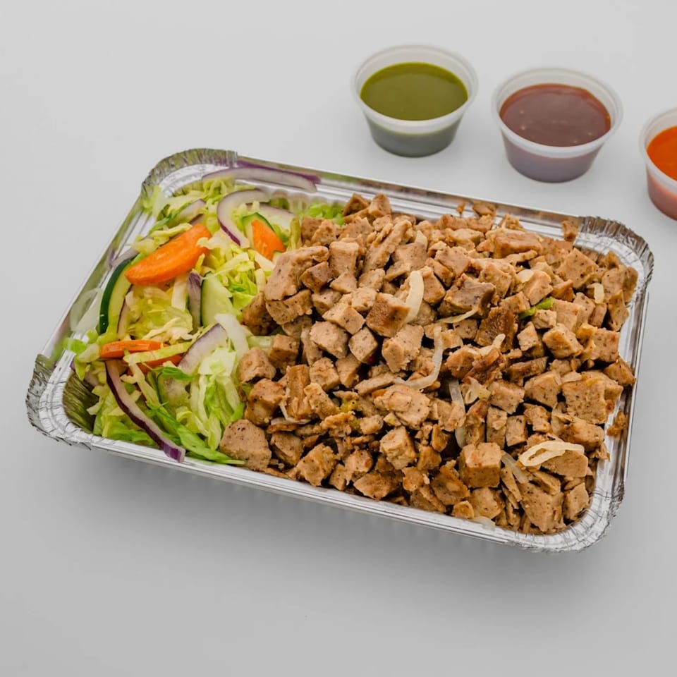 Halal chicken and salad in a foil container with three small sauce cups on the side.